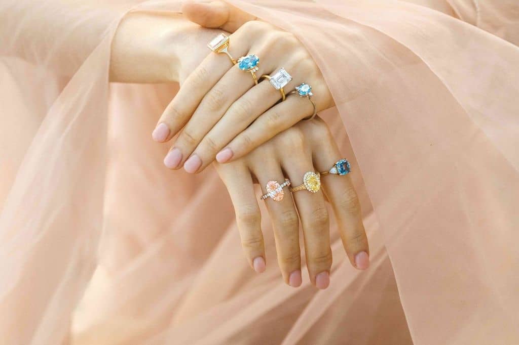 a model wearing colored diamond and gemstone rings on several fingers