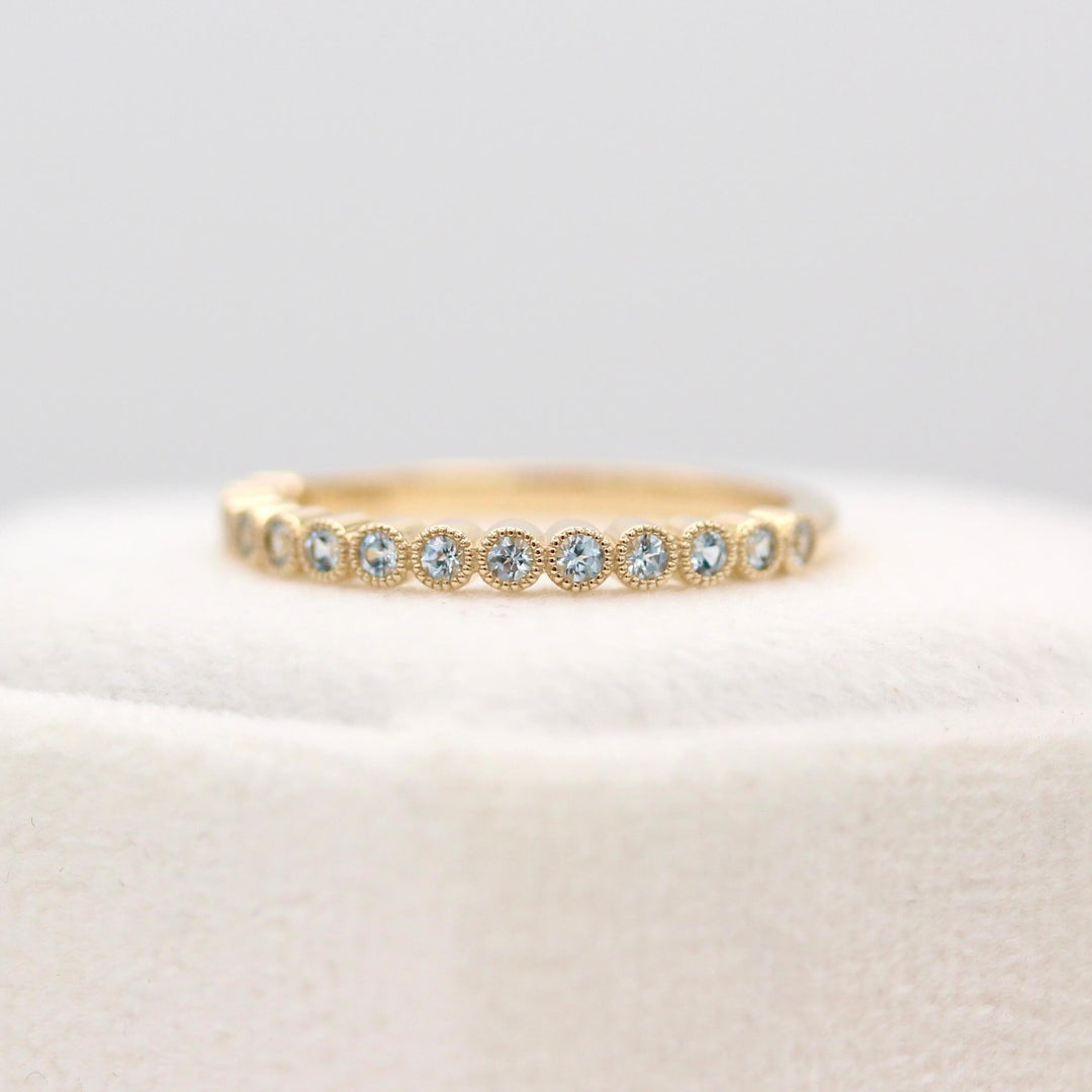 The Florence Wedding Band with Aqua Spinel in Yellow Gold atop of a white velvet ring box