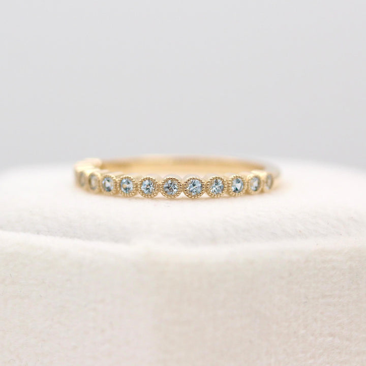 The Florence Wedding Band with Aqua Spinel in Yellow Gold atop of a white velvet ring box