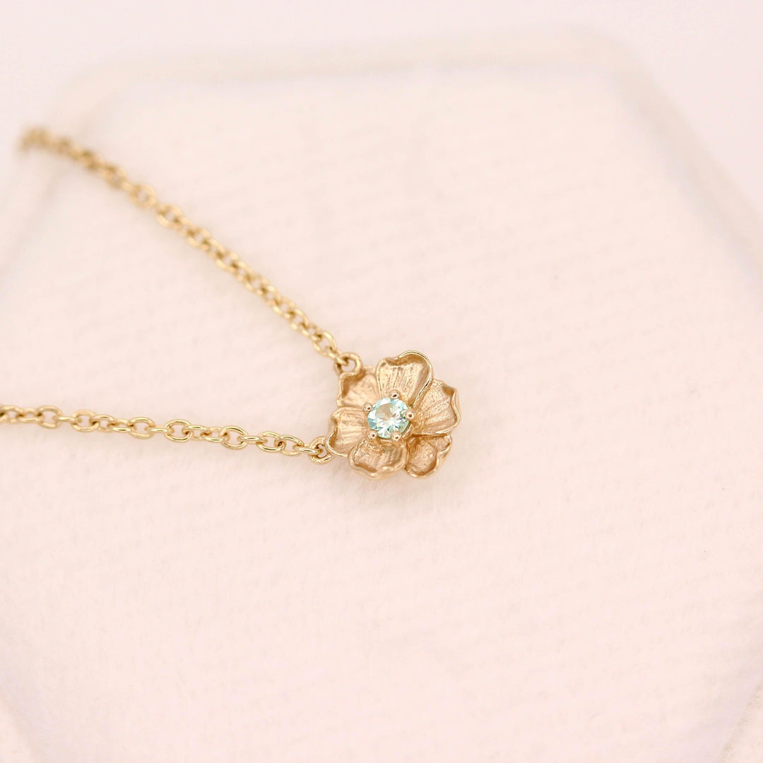 The March Birthstone Poppy Necklace with Aqua Spinel in Yellow Gold against a white velvet ring box