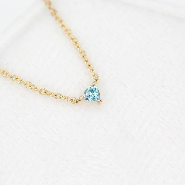 The March Tiny Trillion Birthstone Necklace with Aqua Spinel in Yellow Gold atop of a white velvet ring box