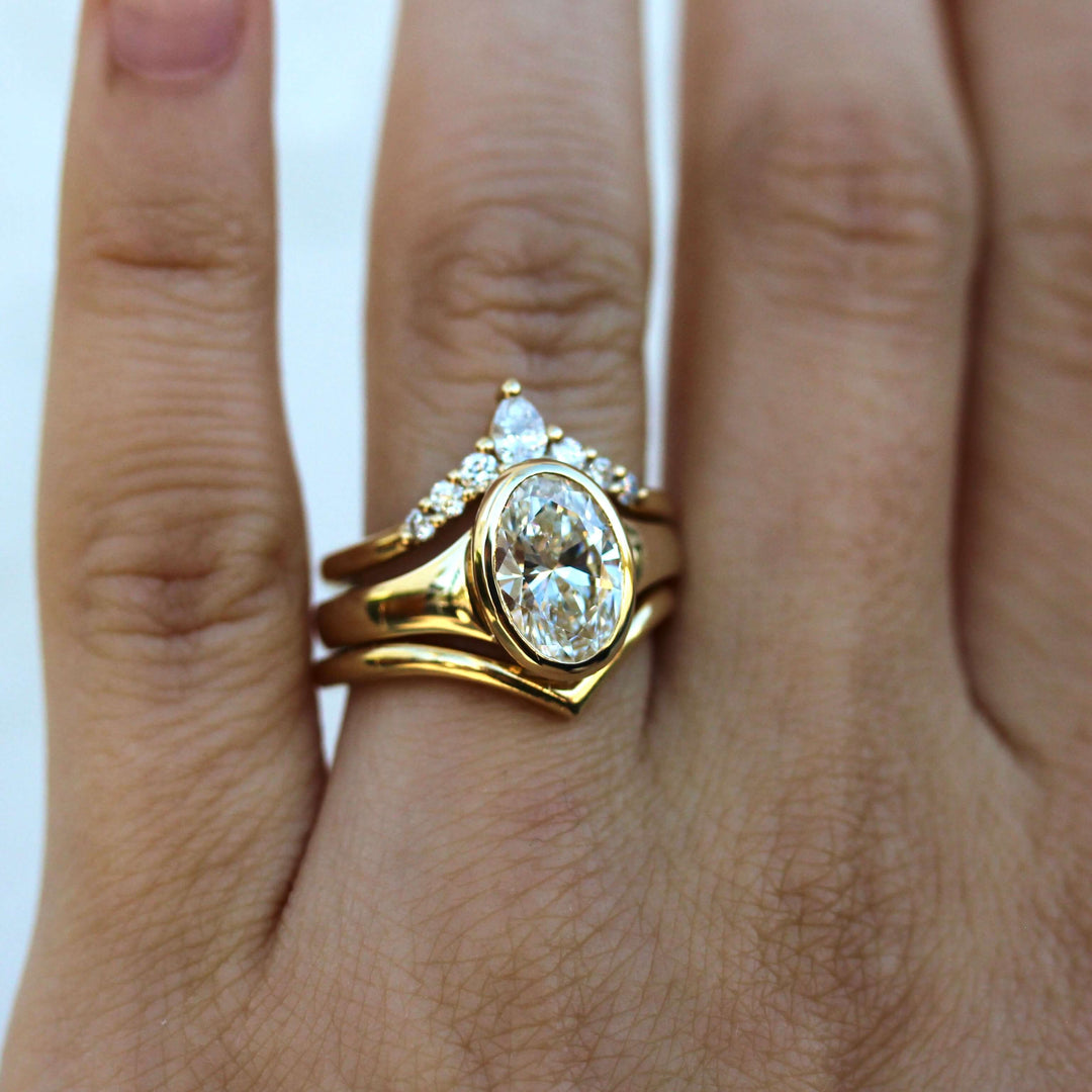 The Billie Ring (Oval) in Yellow Gold with 2ct Lab-Grown Diamond modeled on a hand stacked with the Tiara and V wedding bands in yellow gold