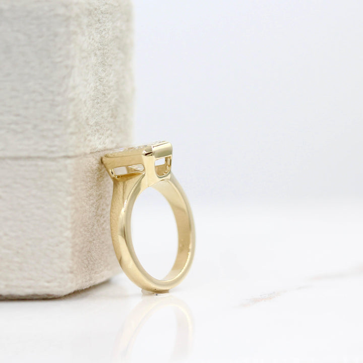 The Billie Ring (Radiant) in Yellow Gold with 2ct LGD leaning against a white velvet ring box