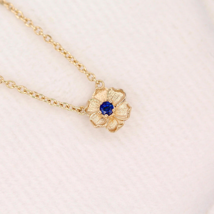 The September Birthstone Poppy Necklace with Blue Sapphire in Yellow Gold against a white velvet ring box