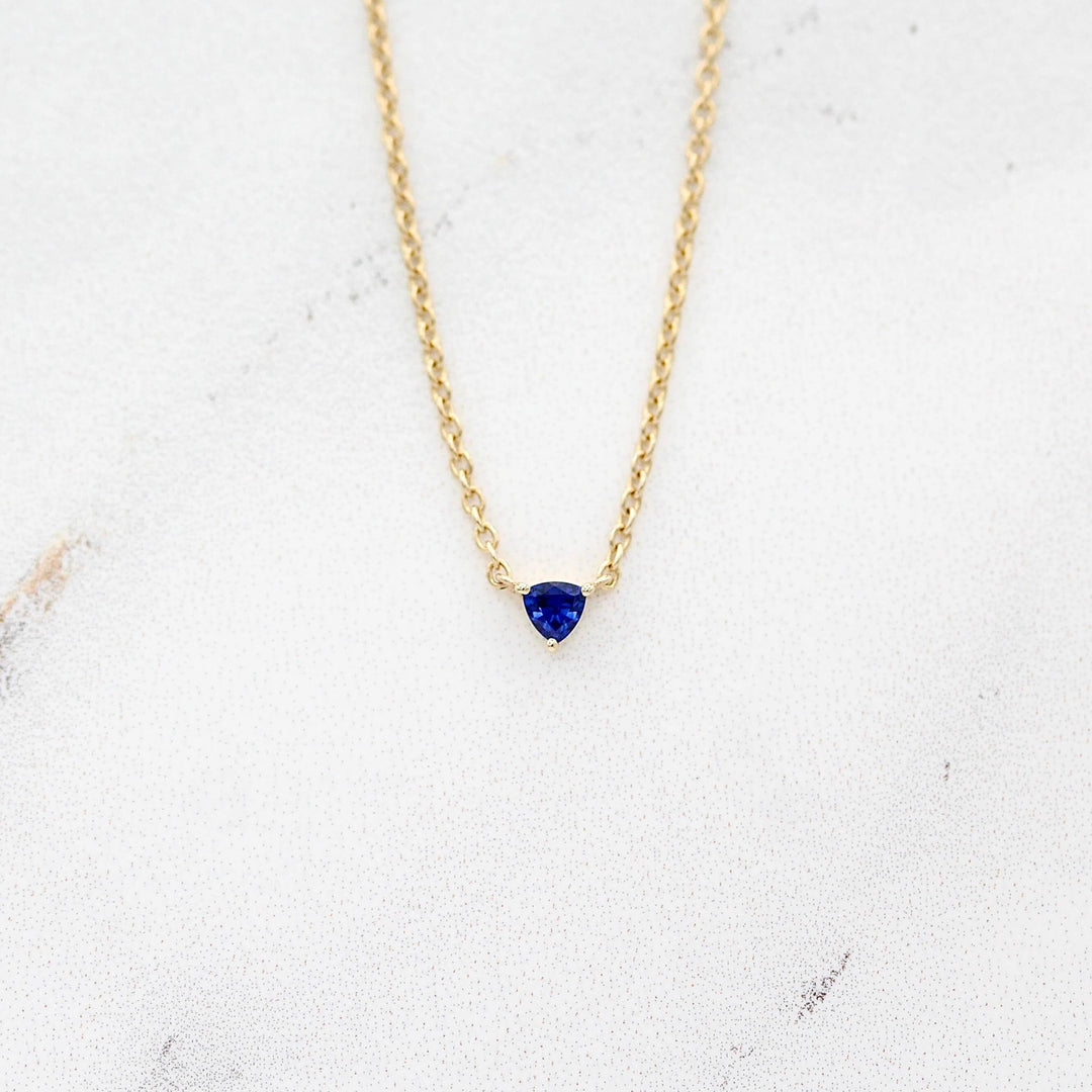 The September Birthstone Tiny Trillion Necklace with Blue Sapphire in Yellow Gold against a white background