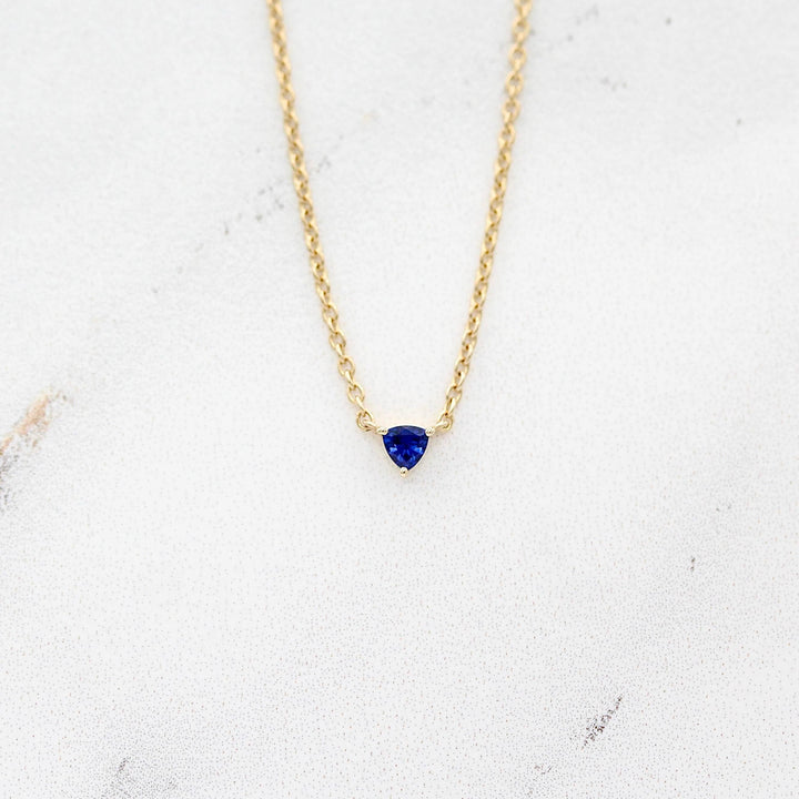 The September Birthstone Tiny Trillion Necklace with Blue Sapphire in Yellow Gold against a white background