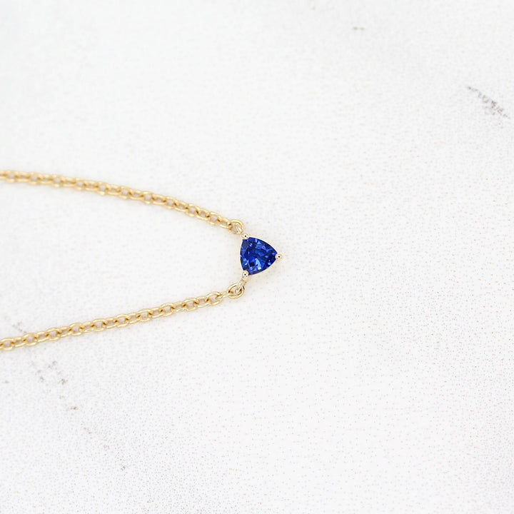 The September Birthstone Tiny Trillion Necklace with Blue Sapphire in Yellow Gold against a white background