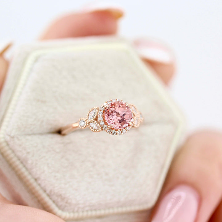 The Cate Ring (Round) in Rose Gold with 1ct Peachy-Pink Created Sapphire in a white velvet ring box held by a hand