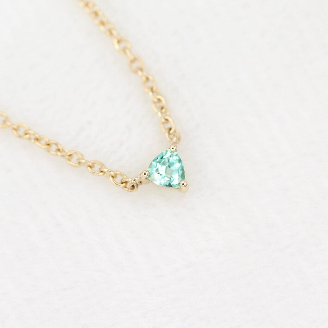 The August Birthstone Tiny Trillion Necklace with Chrysoberyl in Yellow Gold against a white velvet ring box