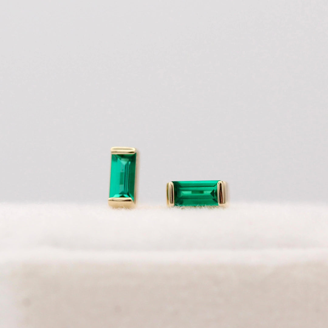 The May Baguette Birthstone Earrings with Emerald in Yellow Gold atop of a white velvet ring box