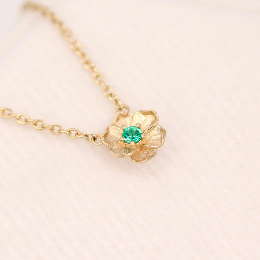 The May Birthstone Poppy Necklace with Emerald in Yellow Gold against a white velvet ring box