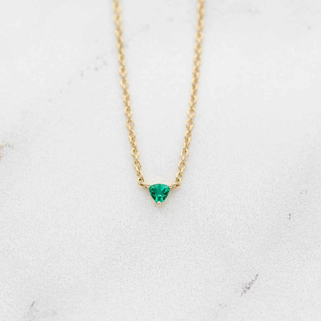 The May Birthstone Tiny Trillion Necklace with Emerald in Yellow Gold against a white background