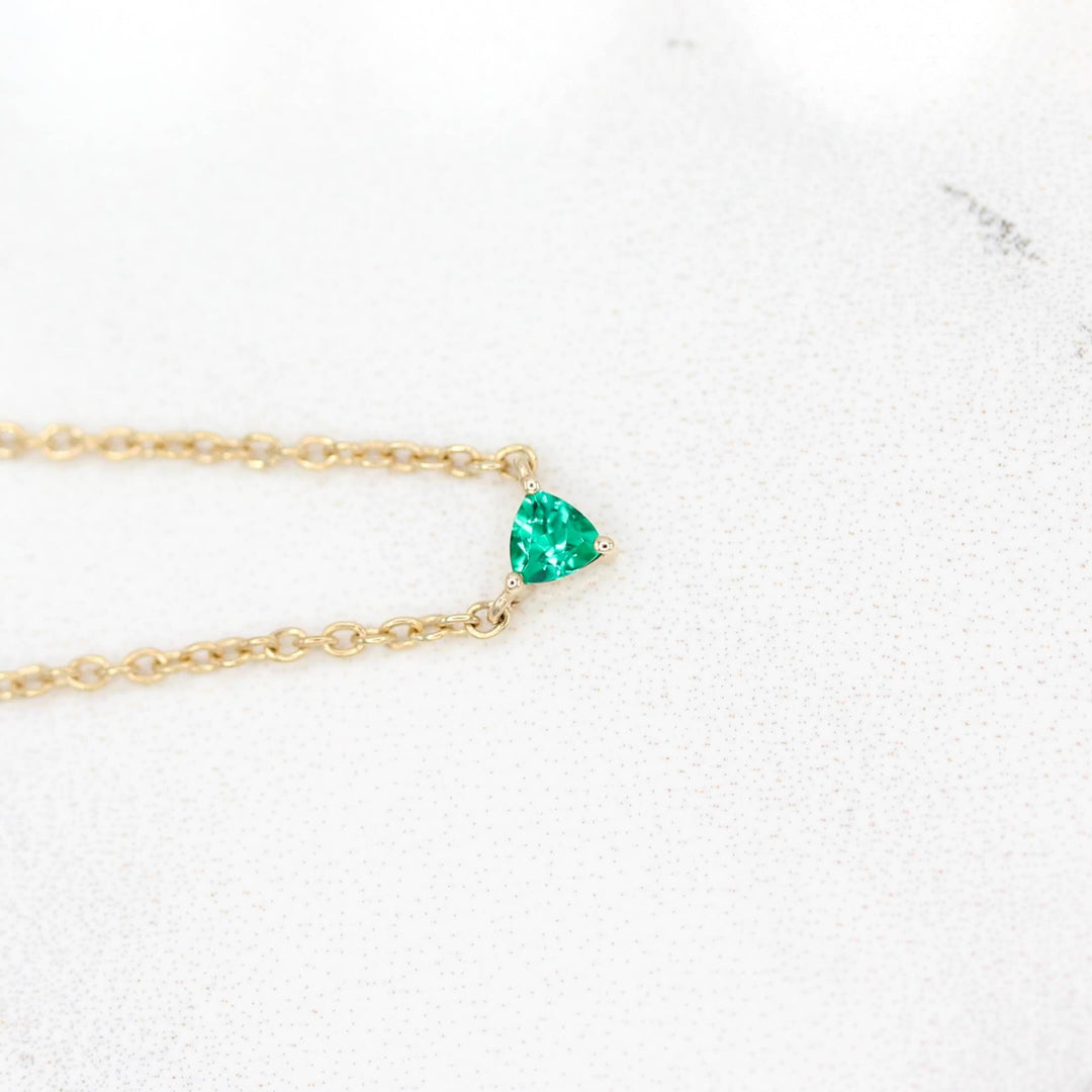 The May Birthstone Tiny Trillion Necklace with Emerald in Yellow Gold against a white background