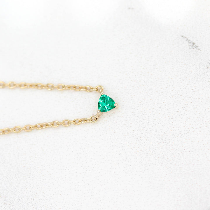 The May Birthstone Tiny Trillion Necklace with Emerald in Yellow Gold against a white background