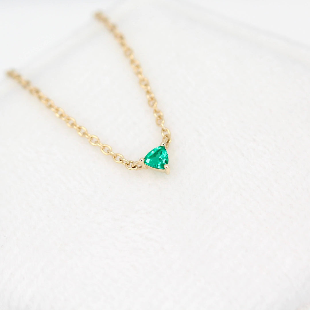 The May Birthstone Tiny Trillion Necklace with Emerald in Yellow Gold against a white background