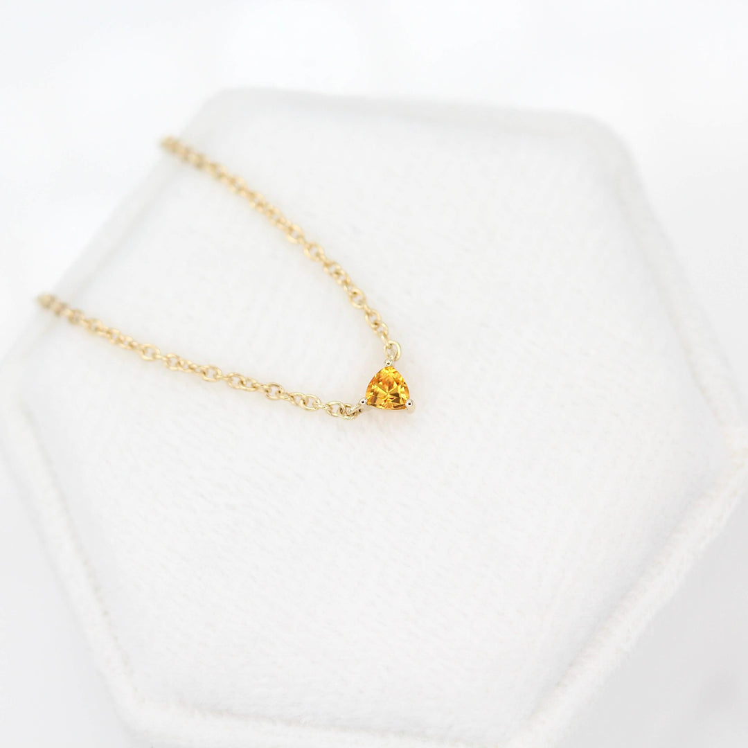 The November Birthstone Tiny Trillion Necklace with Gold Sapphire in Yellow Gold against a white velvet ring box