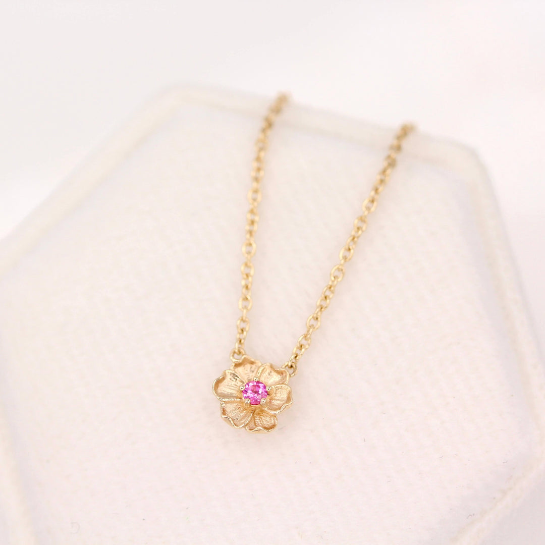 The January Birthstone Poppy Necklace with Padparadcha Sapphire in Yellow Gold atop of a white velvet ring box