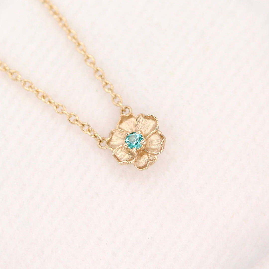 The December Birthstone Poppy Necklace with Paraiba Spinel in Yellow Gold against a white velvet ring box