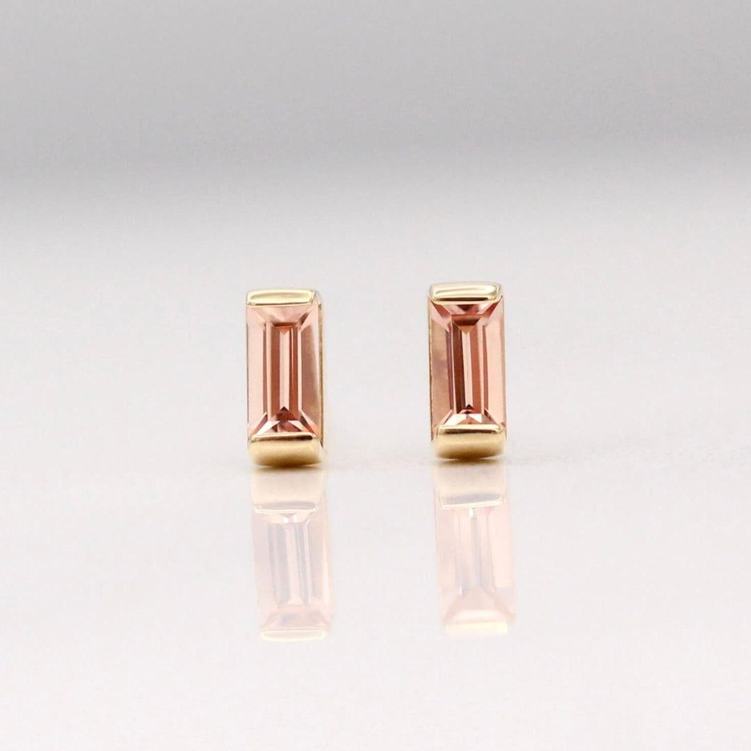 The October Baguette Birthstone Earrings with Peachy-Pink Sapphire in Yellow Gold against a white background