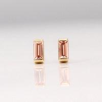 The October Baguette Birthstone Earrings with Peachy-Pink Sapphire in Yellow Gold against a white background