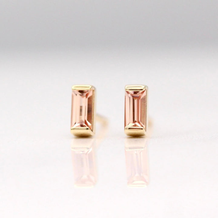 The October Baguette Birthstone Earrings with Peachy-Pink Sapphire in Yellow Gold against a white background