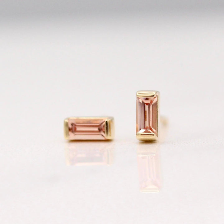 The October Baguette Birthstone Earrings with Peachy-Pink Sapphire in Yellow Gold against a white background