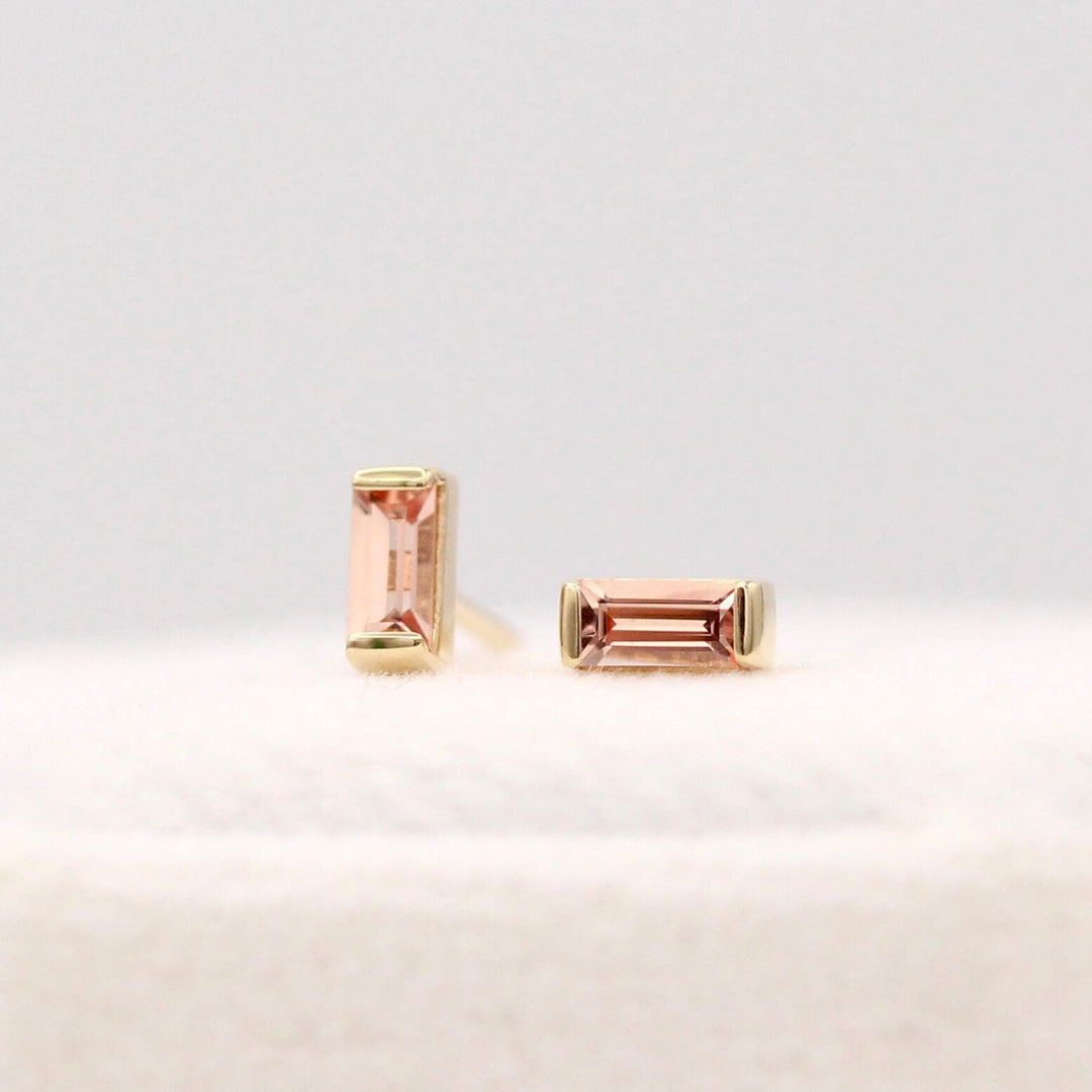 The October Baguette Birthstone Earrings with Peachy-Pink Sapphire in Yellow Gold atop of a white velvet ring box