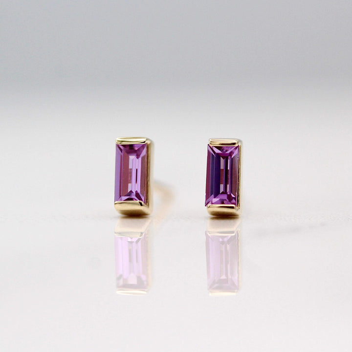 The February Baguette Birthstone Earrings with Purple Sapphire in Yellow Gold against a white background