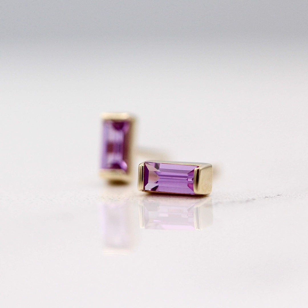 The February Baguette Birthstone Earrings with Purple Sapphire in Yellow Gold against a white background