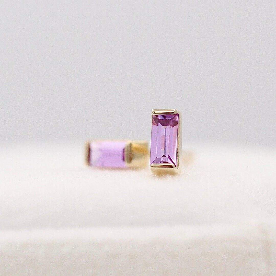 The February Baguette Birthstone Earrings with Purple Sapphire in Yellow Gold atop of a white velvet ring box