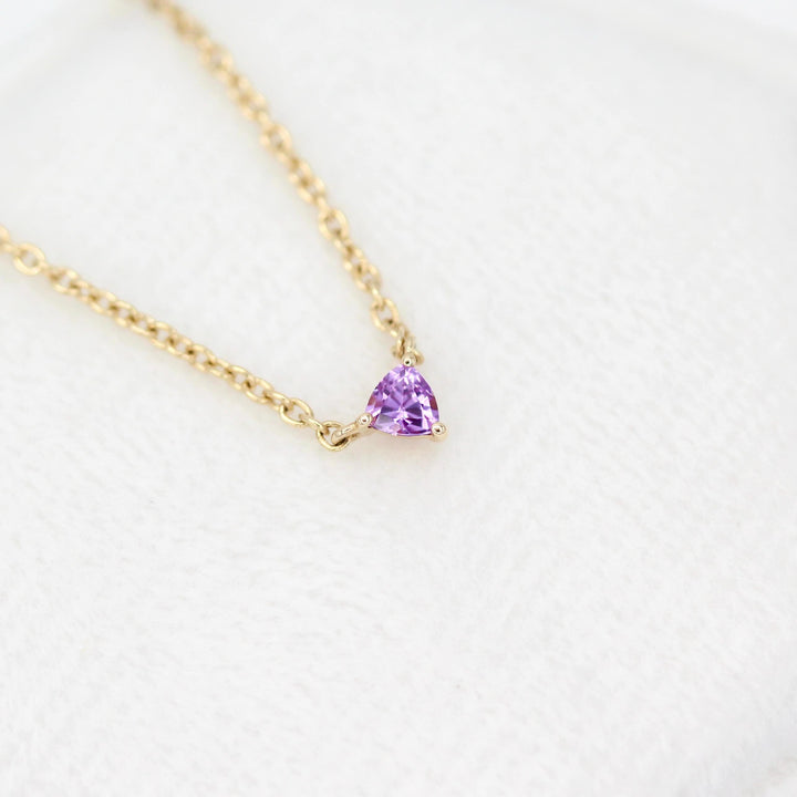 The February Birthstone Tiny Trillion Necklace with Purple Sapphire against a white velvet ring box