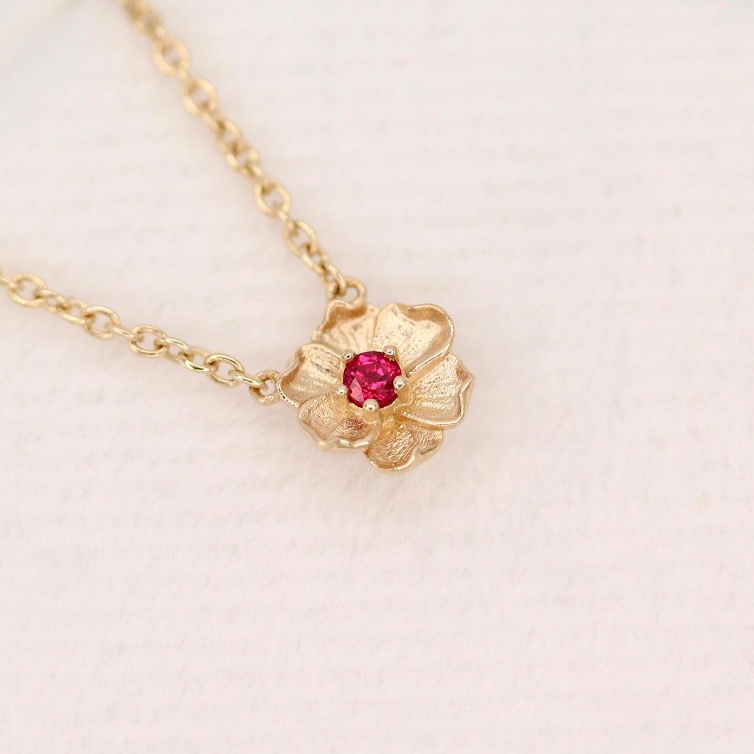 The July Birthstone Poppy Necklace with Ruby in Yellow Gold against a white velvet ring box