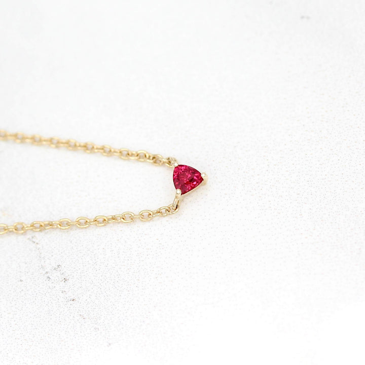 The July Birthstone Tiny Trillion Necklace with Ruby in Yellow Gold against a white background